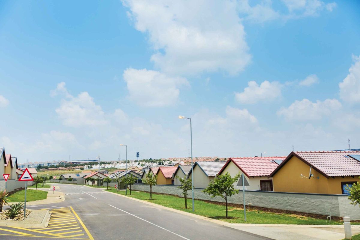 A clear street view of a residential neighbourhood featuring paved roads, street lighting, and well-maintained boundary walls.