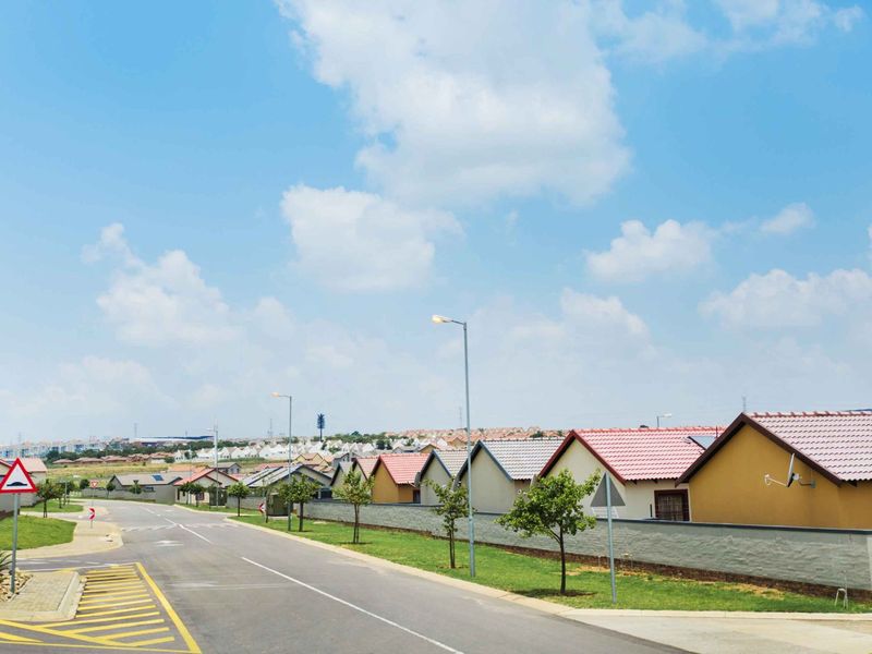 A clear street view of a residential neighbourhood featuring paved roads, street lighting, and well-maintained boundary walls.
