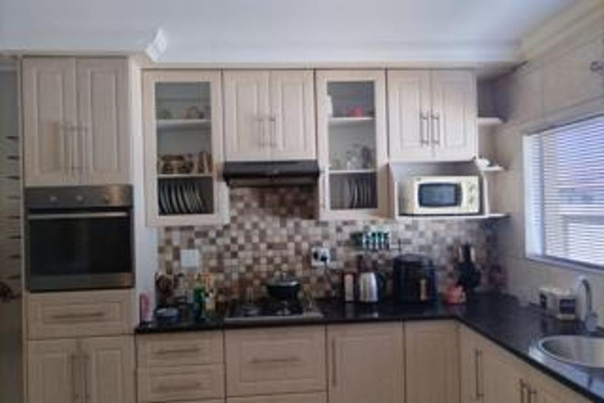 A functional kitchen featuring shaker-style cabinetry, granite countertops, a mosaic tile backsplash, and integrated appliances including an oven, hob, and microwave.