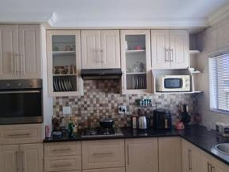 A functional kitchen featuring shaker-style cabinetry, granite countertops, a mosaic tile backsplash, and integrated appliances including an oven, hob, and microwave.