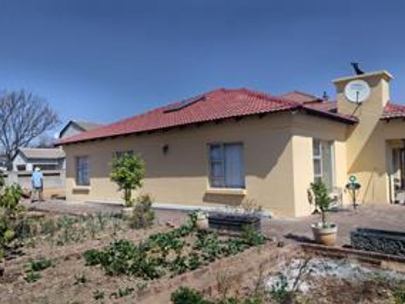 Rear view of the house featuring a tiled roof, solar water heating system, paved patio area, and established garden beds.