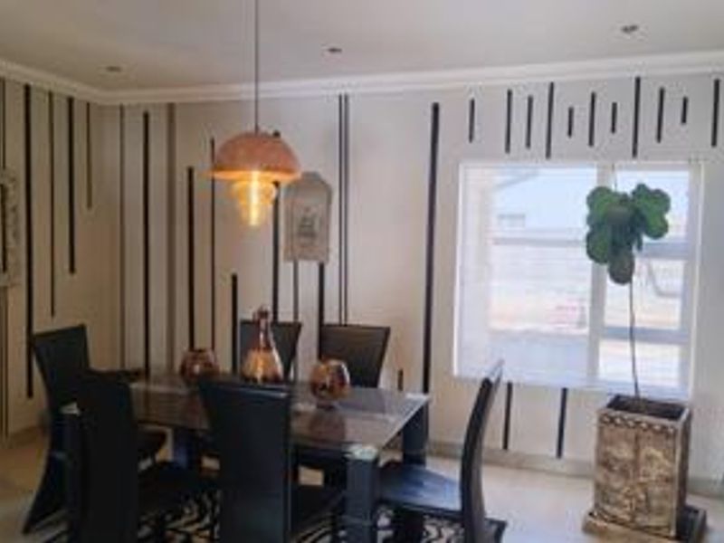 A well-lit dining room featuring decorative wall paneling, recessed ceiling lighting, and a large window providing natural light.