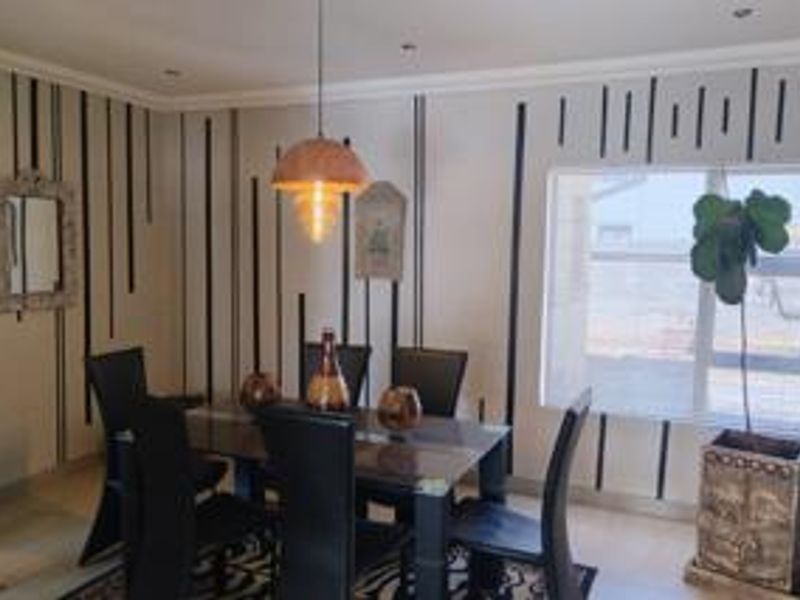 A dining room featuring a pendant light fixture, recessed downlights, and a window with blinds, finished with decorative wall detailing.