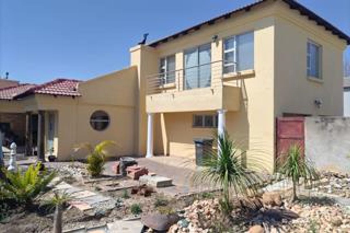 Rear view of a two-story house featuring a balcony, paved patio area, and established garden space.