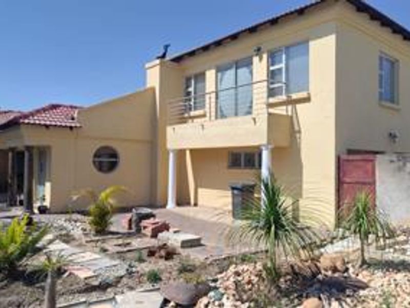 Rear view of a two-story house featuring a balcony, paved patio area, and established garden space.