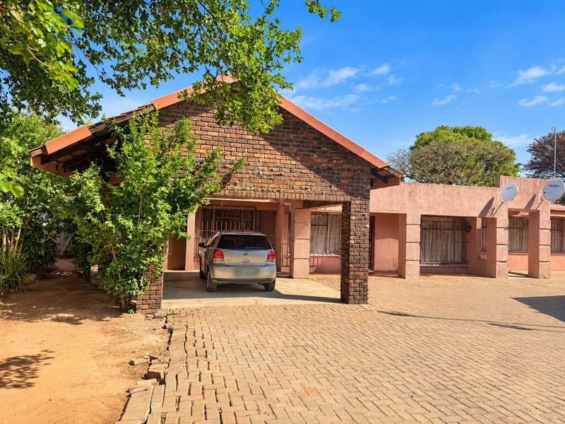 Front elevation of a single-story house featuring a brick facade, covered carport, and paved driveway area.
