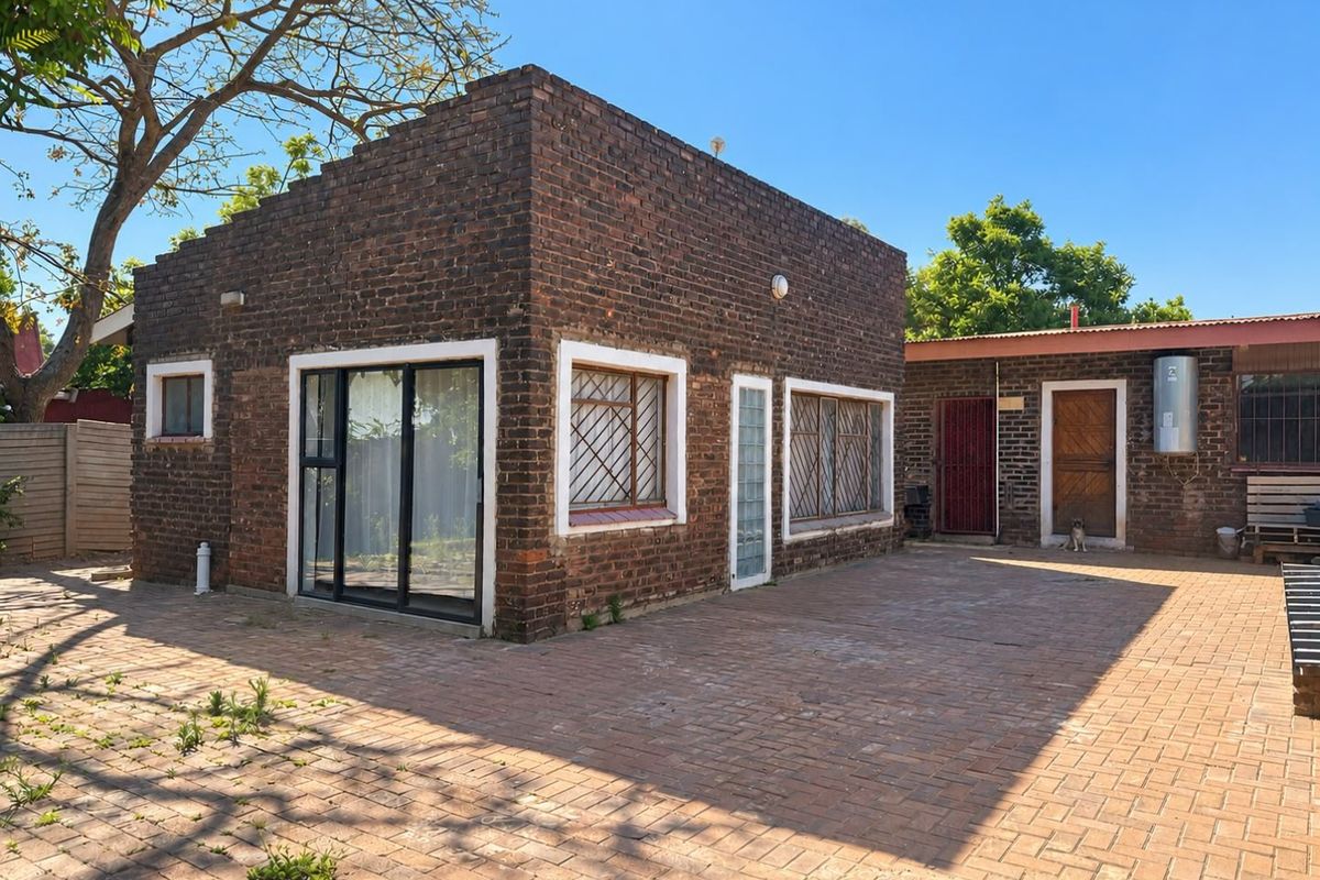 Rear exterior view of a brick house featuring a paved courtyard, sliding glass doors, and security-fitted windows.