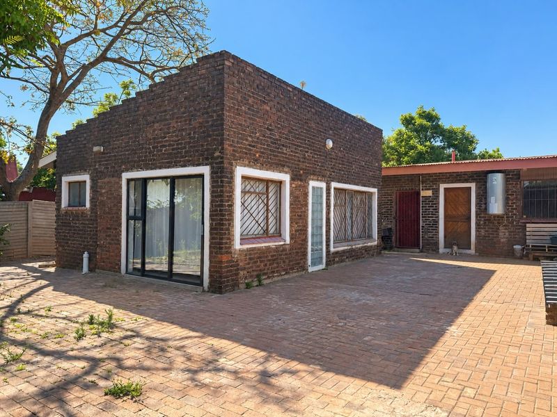Rear exterior view of a brick house featuring a paved courtyard, sliding glass doors, and security-fitted windows.