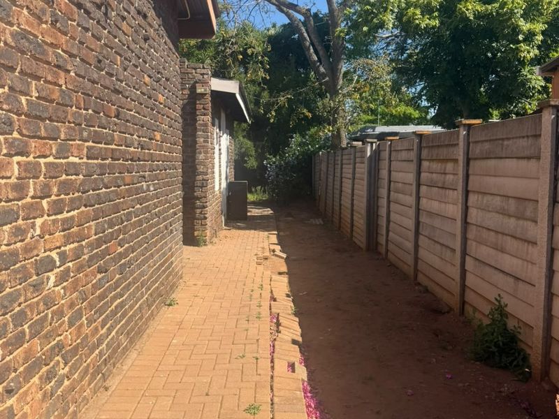 A side exterior view of the property featuring a brick wall, a paved walkway, and a precast concrete boundary wall.