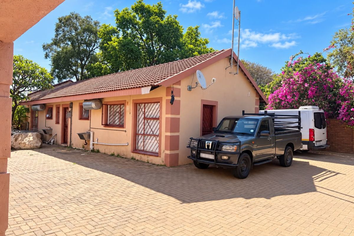 Rear exterior view of the house featuring a paved driveway, tiled roof, security bars on windows, and external utility fixtures.