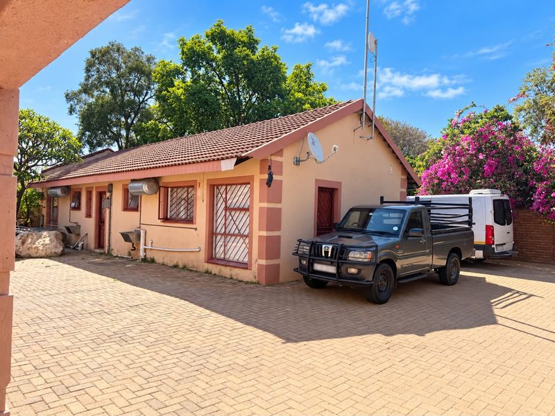 Rear exterior view of the house featuring a paved driveway, tiled roof, security bars on windows, and external utility fixtures.