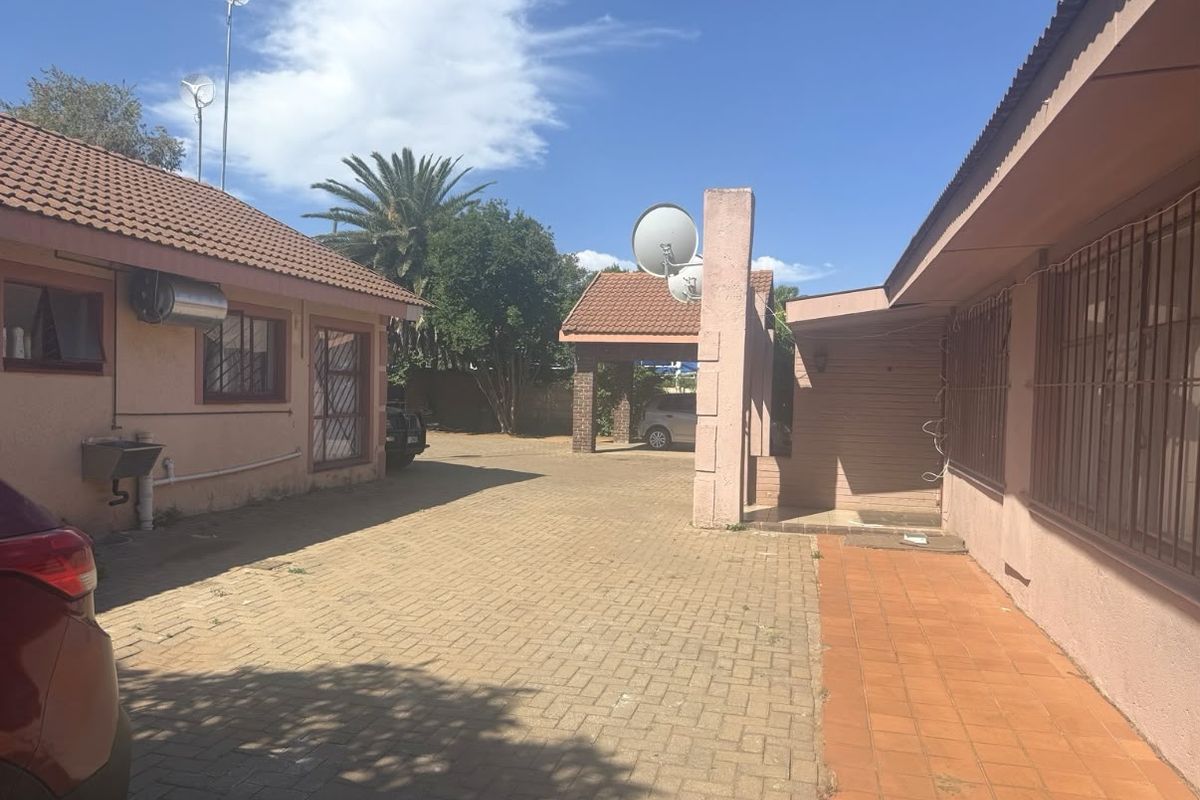 Rear exterior view featuring a paved driveway, carport, and tiled roof structures with security bars on windows.