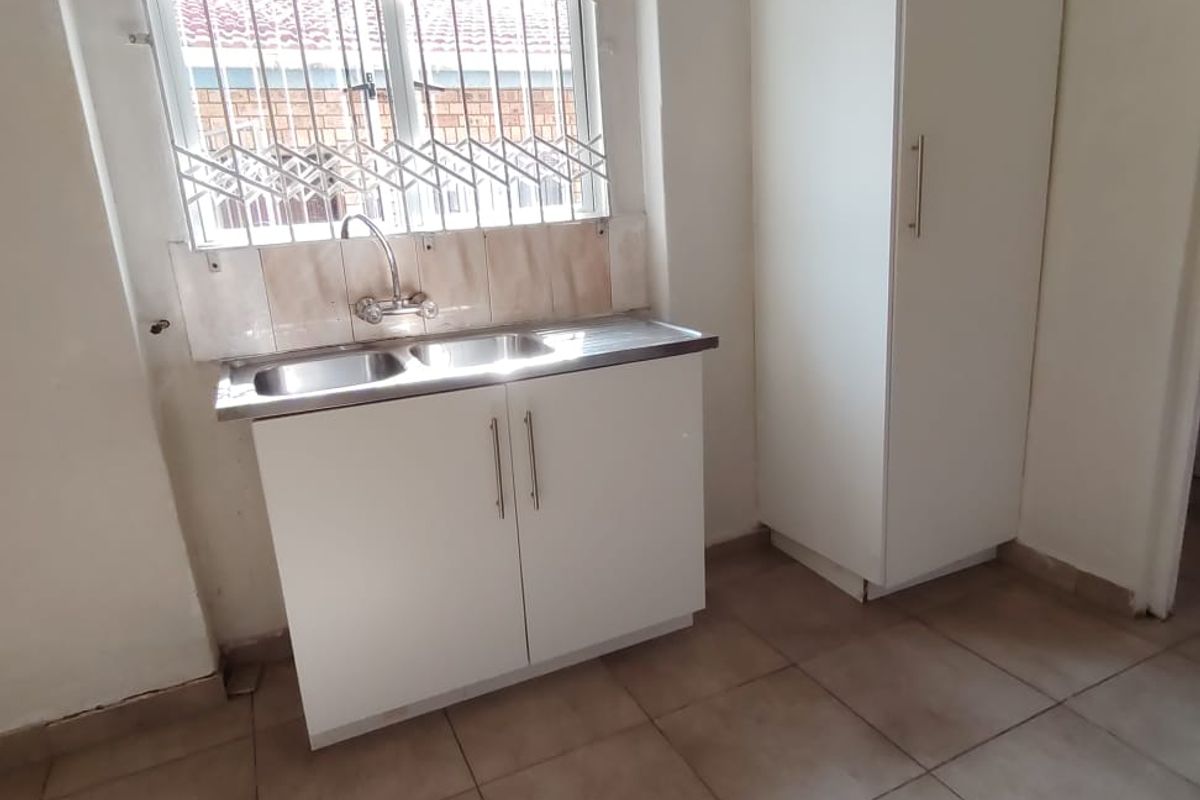 A functional scullery or utility area featuring a stainless steel double sink, built-in cabinetry, a tall pantry cupboard, and tiled flooring.