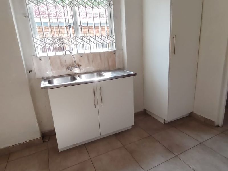 A functional scullery or utility area featuring a stainless steel double sink, built-in cabinetry, a tall pantry cupboard, and tiled flooring.