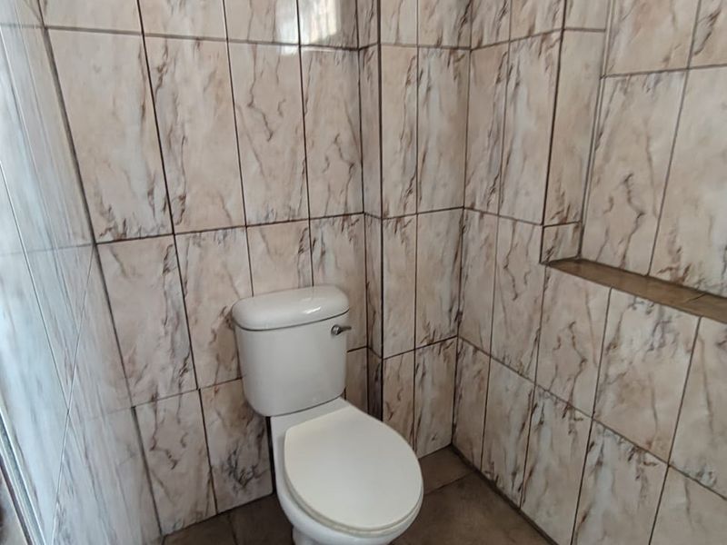 A small bathroom featuring full-height marble-effect wall tiling, a tiled floor, and a built-in recessed wall niche.