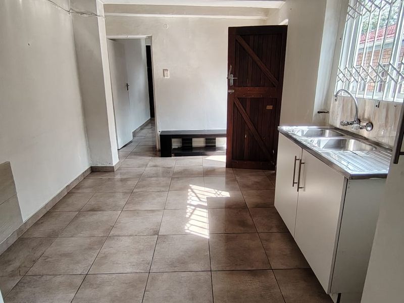 A compact, empty kitchen area featuring tiled flooring, a stainless steel sink unit, and direct access to an adjacent room.