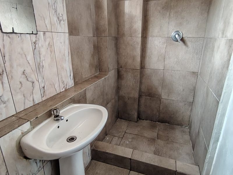 A compact bathroom featuring a pedestal basin and a walk-in shower area with tiled finishes throughout.