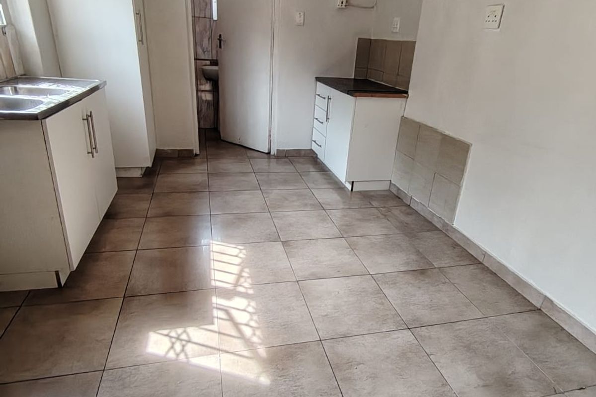 A compact, empty kitchen featuring tiled flooring, basic built-in cabinetry, and a stainless steel sink, requiring cosmetic updates and finishing touches.
