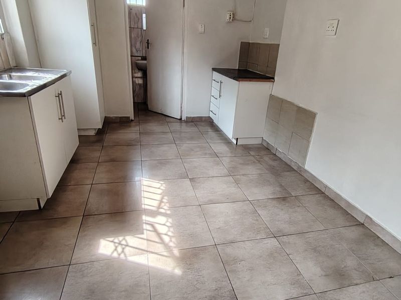 A compact, empty kitchen featuring tiled flooring, basic built-in cabinetry, and a stainless steel sink, requiring cosmetic updates and finishing touches.