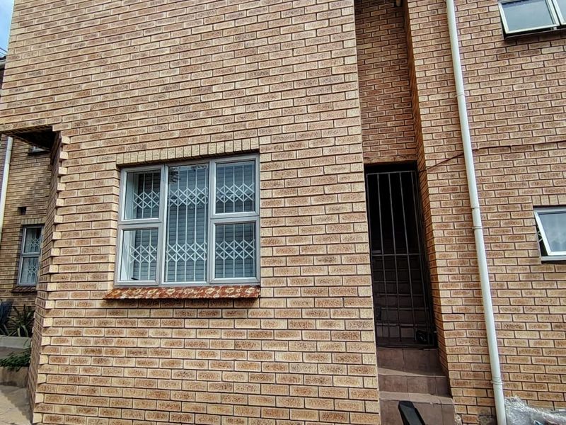 Rear exterior view of a face brick house featuring security bars on windows, a paved patio area, and a side entrance.
