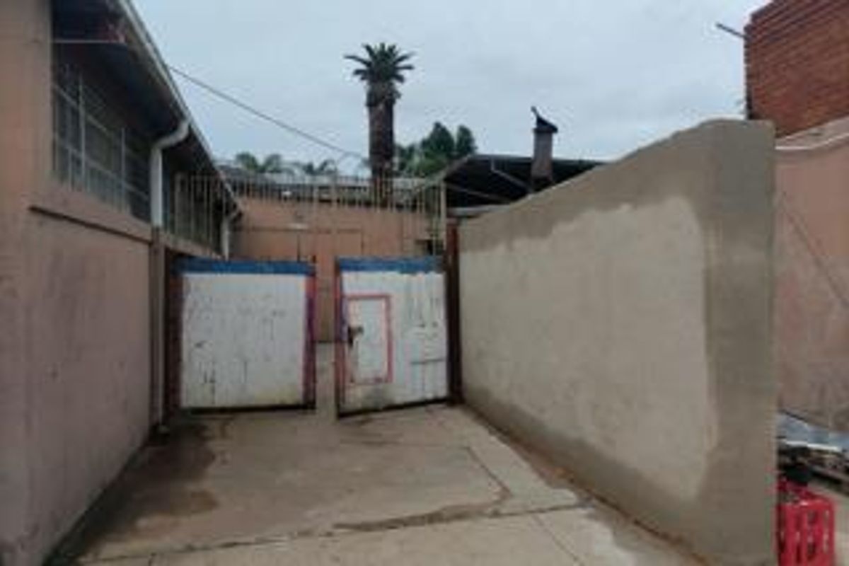 Rear exterior area featuring a concrete driveway, boundary wall, and metal security gate access.