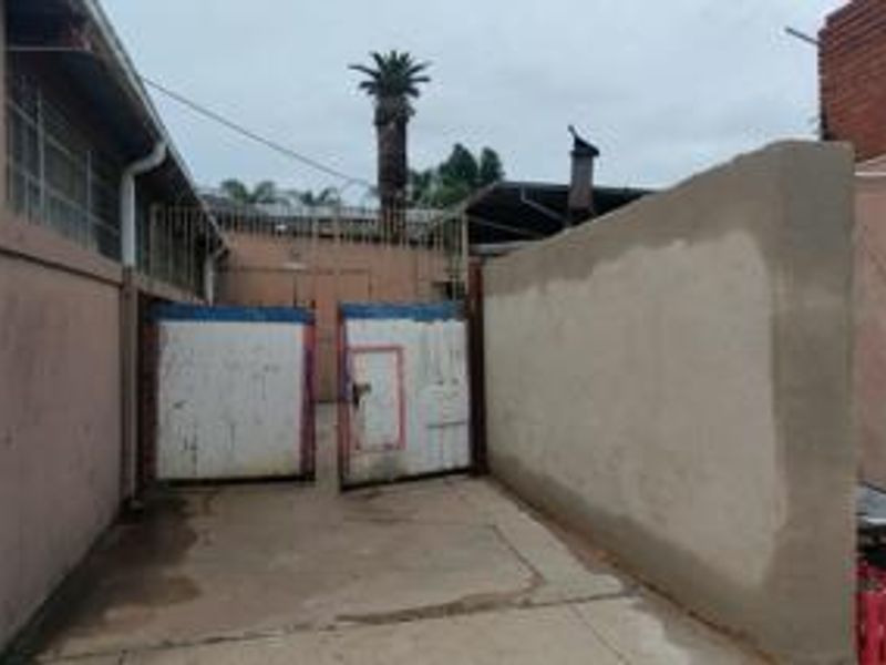 Rear exterior area featuring a concrete driveway, boundary wall, and metal security gate access.