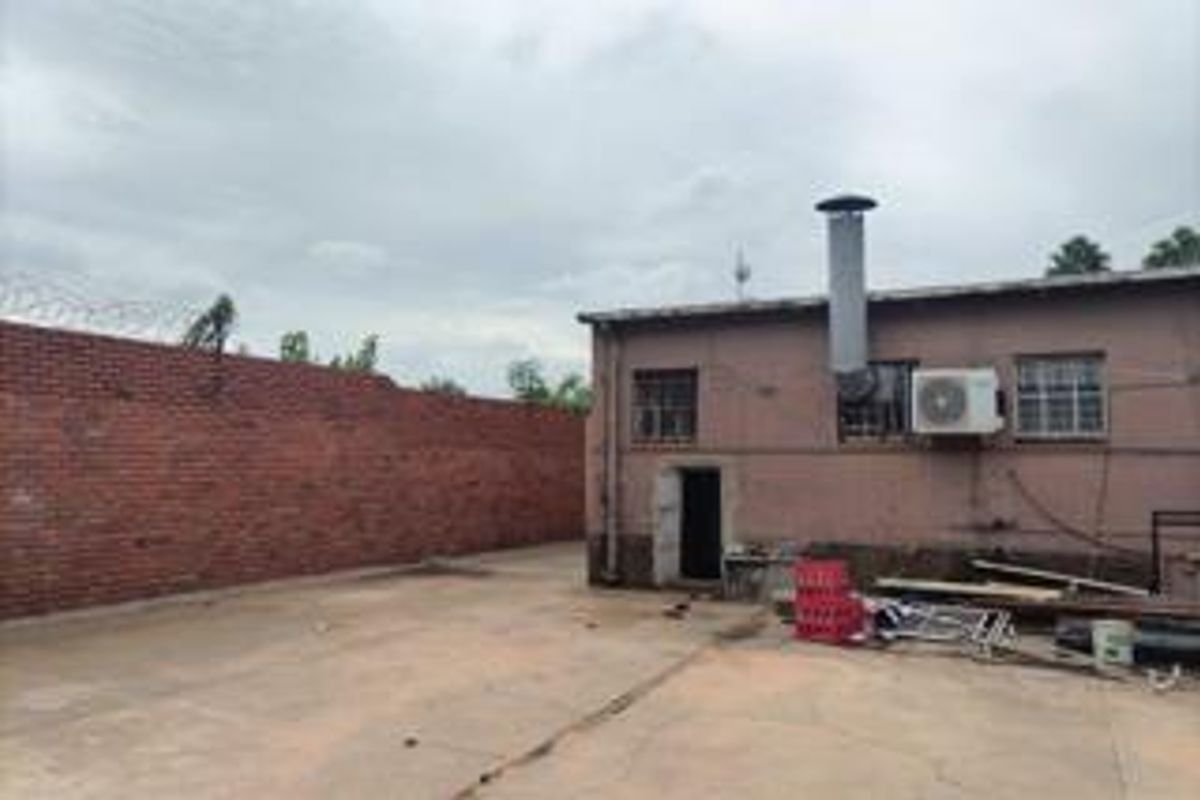 Rear exterior area of a commercial property featuring a brick boundary wall with security fencing, concrete paving, and external building infrastructure.