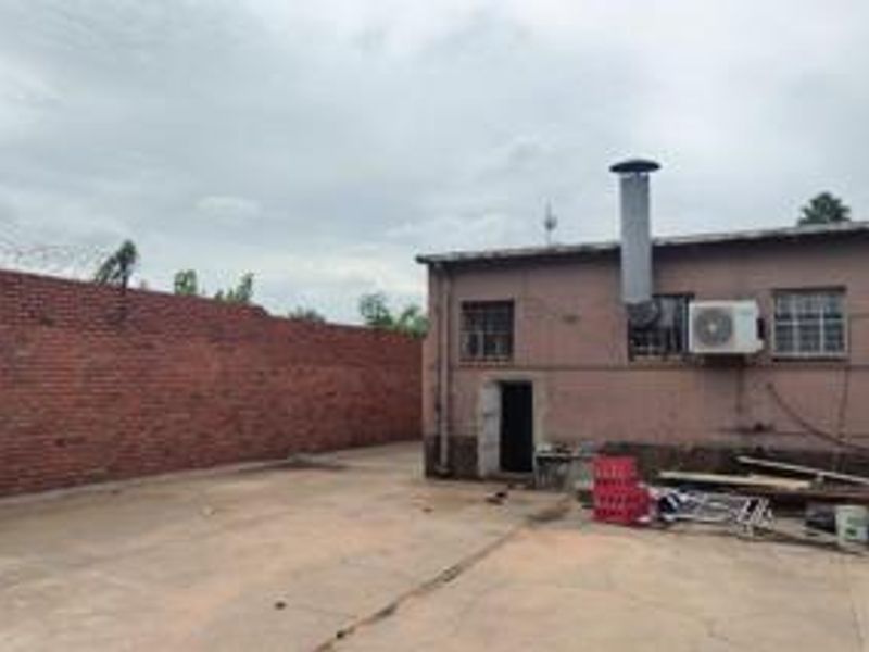 Rear exterior area of a commercial property featuring a brick boundary wall with security fencing, concrete paving, and external building infrastructure.