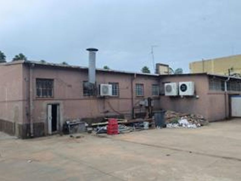 Rear exterior view of a commercial building featuring concrete yard space, external air conditioning units, and industrial access points.