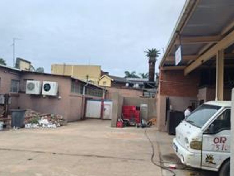 Rear commercial yard area featuring a concrete surface, covered loading bay, and external air conditioning units attached to the building facade.