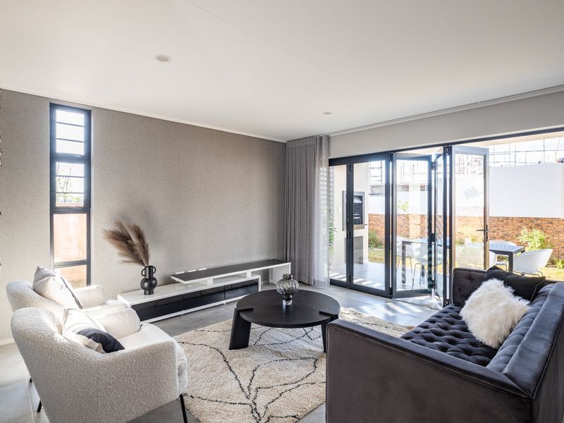 Modern living room featuring tiled floors, recessed lighting, and large black aluminium stacker doors providing seamless access to the outdoor patio area.