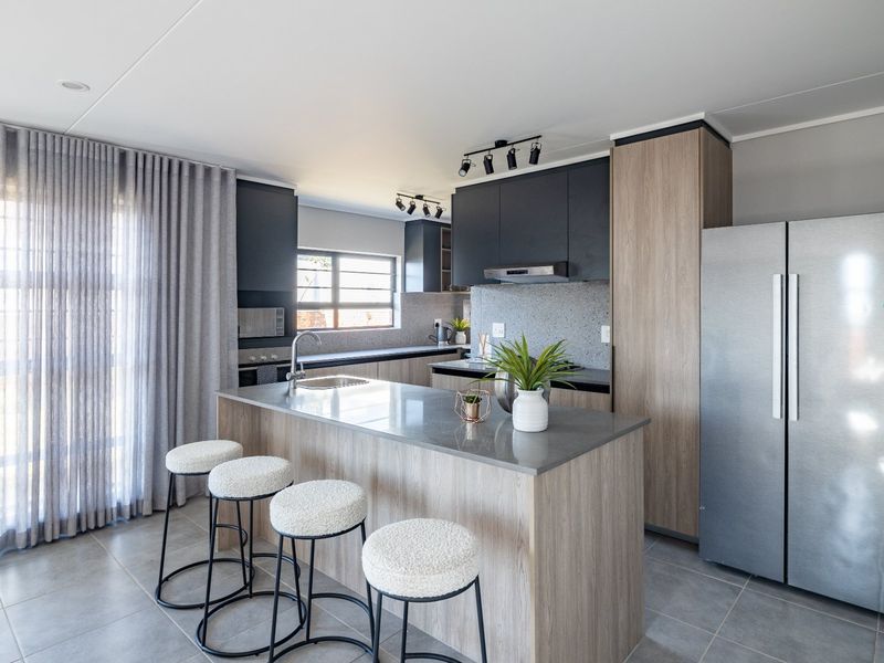 Modern kitchen featuring a central island with stone countertops, sleek two-tone cabinetry, integrated extractor fan, and high-quality tiled flooring.