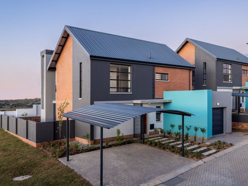 Modern double-story house featuring a brick and painted facade, corrugated metal roof, integrated garage, and a covered carport with a paved driveway.