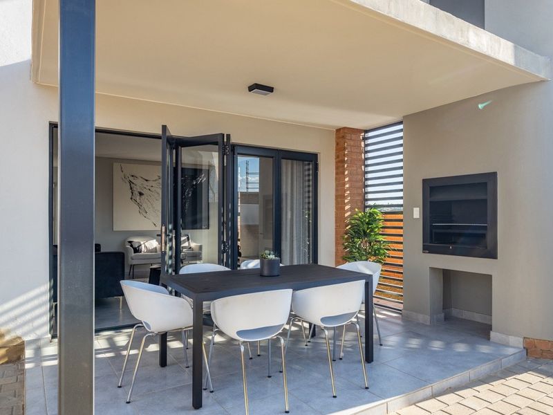 A modern covered patio featuring a built-in braai, tiled flooring, and bi-fold doors that provide seamless access to the interior living space.
