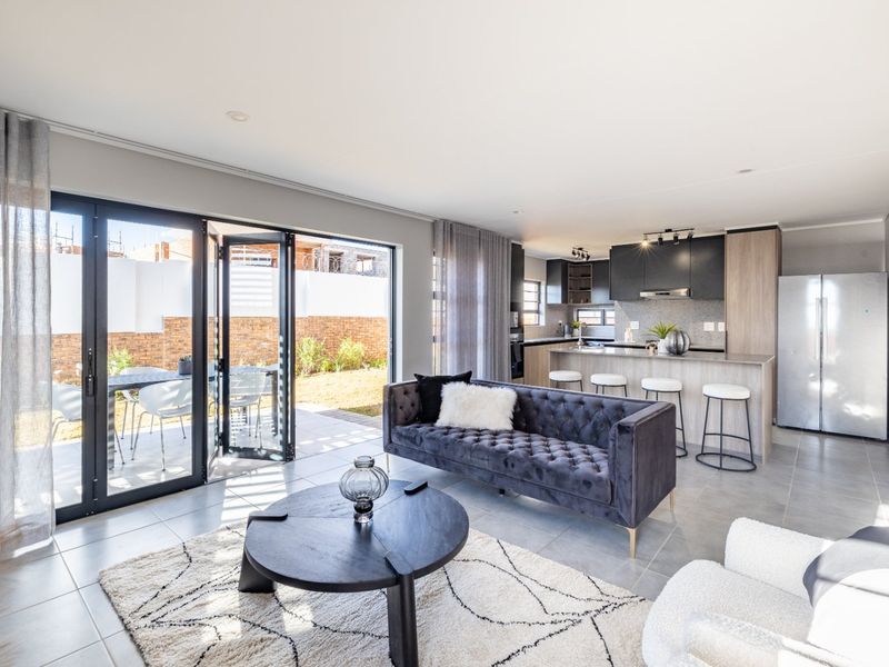 Modern open-plan living area featuring a sleek kitchen with island, tiled floors, and large bi-fold doors opening to a private patio and garden.