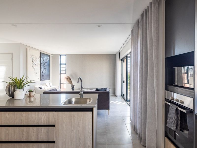Modern open-plan living area featuring a sleek kitchen island with sink, built-in appliances, and seamless flow to the outdoor space through large sliding doors.