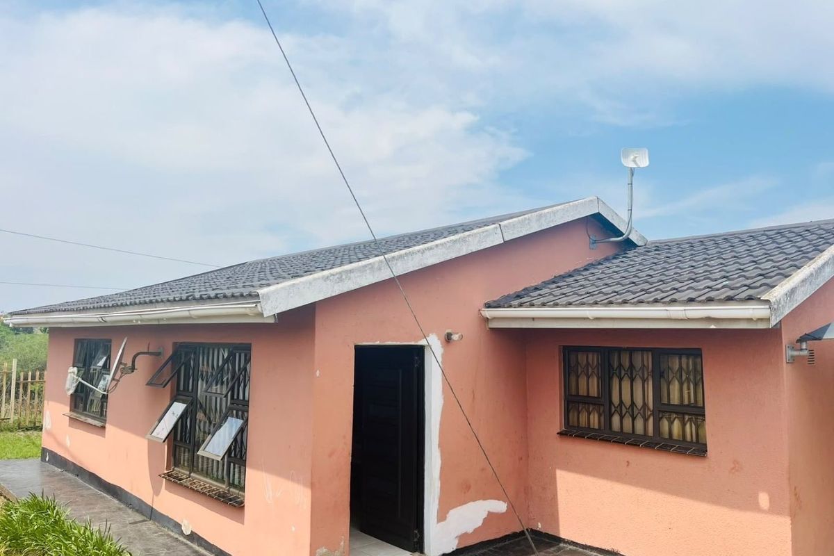Rear exterior view of a single-story house featuring a tiled roof, security bars on windows, and a paved walkway area.