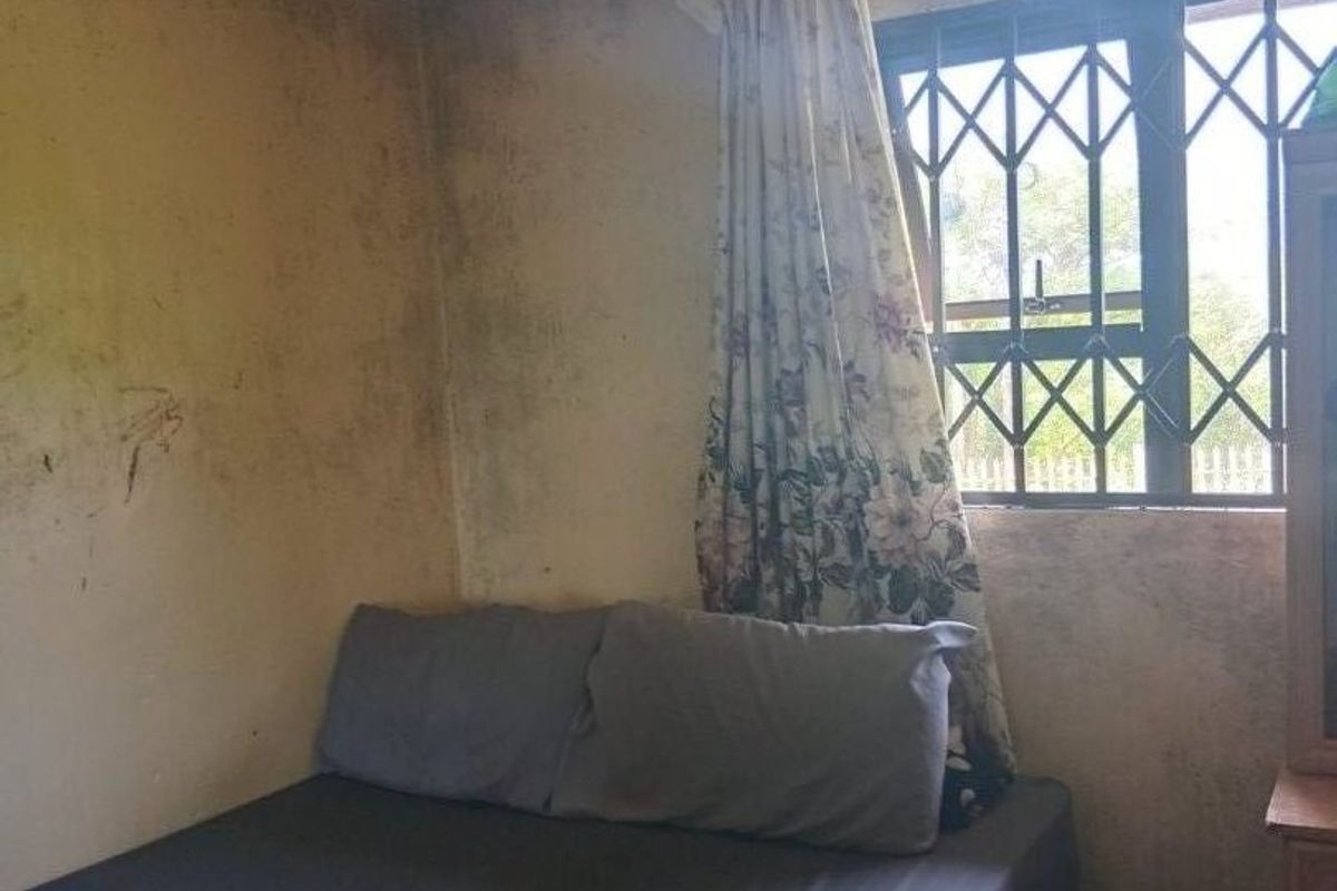 A bedroom featuring tiled flooring and a security gate on the window, currently requiring significant wall repairs and cosmetic refurbishment.