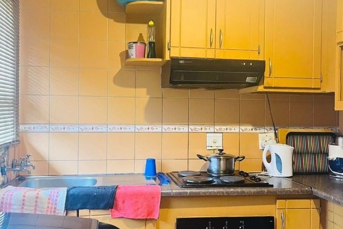 A compact kitchen featuring dated yellow cabinetry, a built-in oven and hob, extractor fan, and tiled backsplash with a stainless steel sink.
