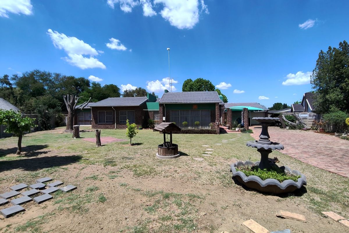 Spacious rear garden featuring a brick house facade, paved driveway, decorative water fountain, and a wishing well set within a large lawn area.