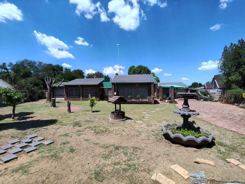 Spacious rear garden featuring a brick house facade, paved driveway, decorative water fountain, and a wishing well set within a large lawn area.