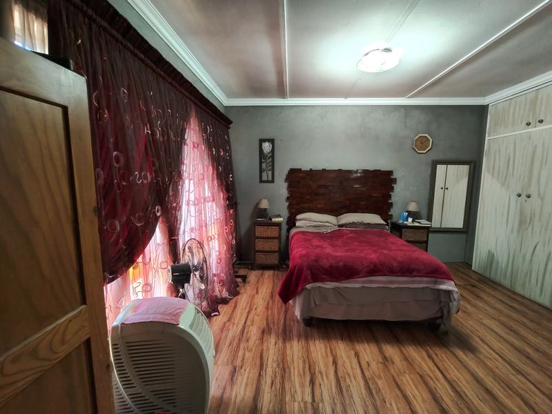 A spacious bedroom featuring laminate flooring, built-in cupboards, and a neutral wall finish, offering a functional layout ready for modern updates.