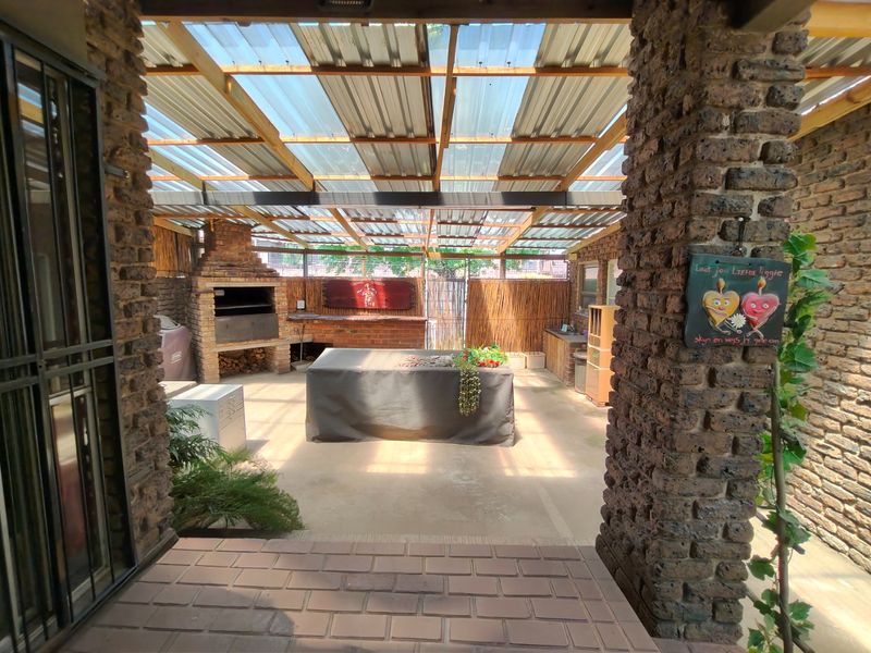 Covered outdoor patio area featuring a built-in brick braai, exposed brick pillars, and a translucent roof, providing a functional space for outdoor entertaining.