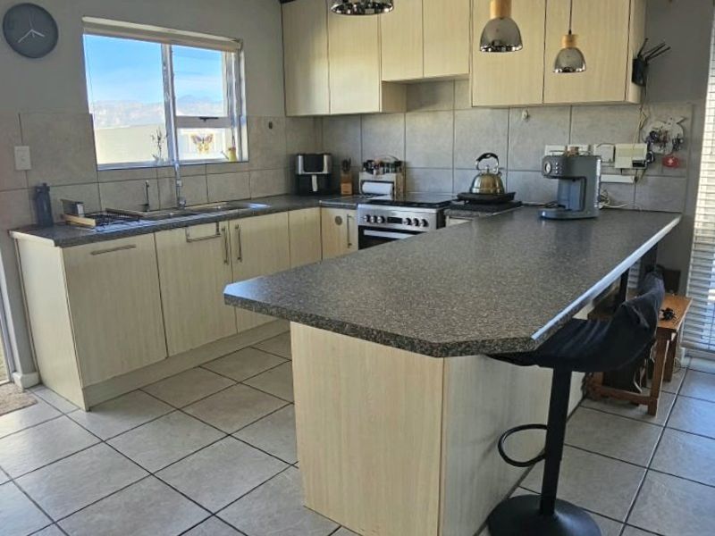 Functional kitchen featuring light wood-finish cabinetry, laminate countertops, a breakfast bar, and tiled flooring with direct access to an outdoor area.