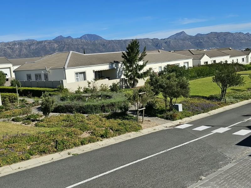 A scenic elevated view of a residential estate featuring well-maintained gardens, paved roads, and a backdrop of mountain ranges.