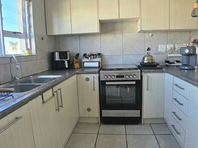 A functional kitchen featuring light-toned laminate cabinetry, granite countertops, a stainless steel double sink, and a freestanding oven with a tiled backsplash.