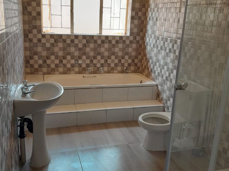 A functional bathroom featuring a pedestal basin, built-in bathtub, separate shower enclosure, and tiled wall finishes.