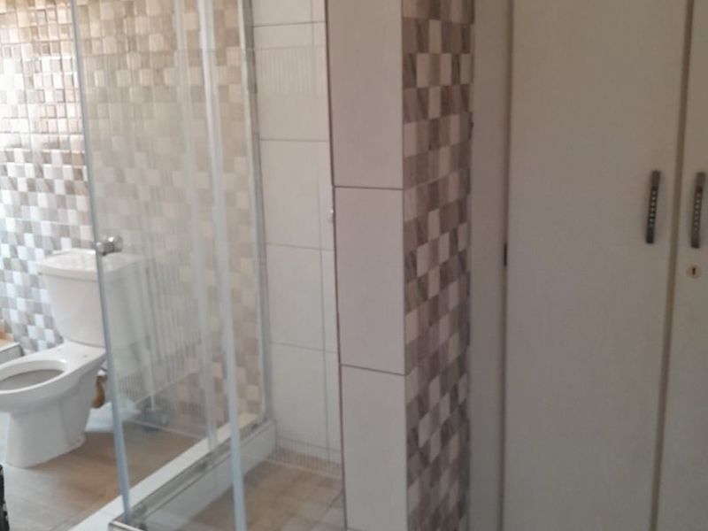A functional bathroom featuring a glass shower enclosure, toilet, and built-in storage cupboard with neutral tiled finishes.