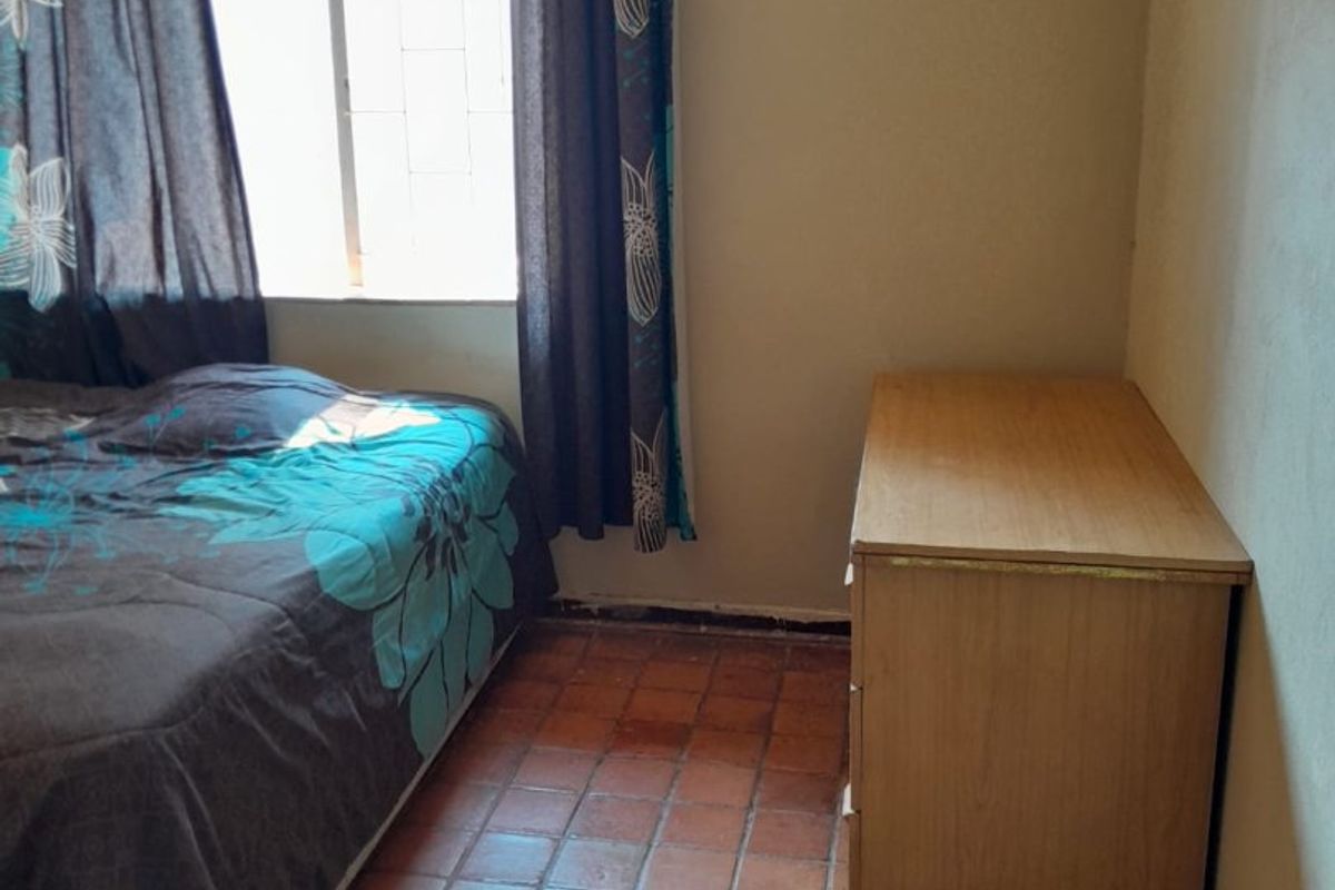 A bedroom featuring terracotta tile flooring and a window with security bars, requiring cosmetic updates to improve the overall aesthetic.