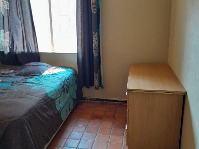 A bedroom featuring terracotta tile flooring and a window with security bars, requiring cosmetic updates to improve the overall aesthetic.